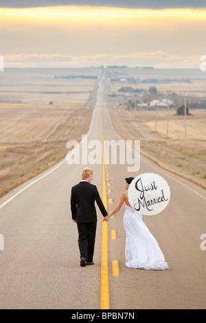 Three Hills, Alberta, Canada ; une femme et un homme marchant sur une route avec bride holding a parasol avec 'juste' mariés sur elle Banque D'Images