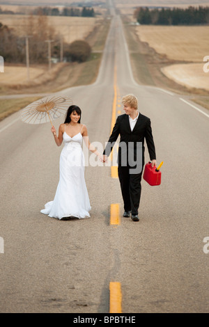 Three Hills, Alberta, Canada ; une femme et un homme marchant sur un chemin rural tenant un jerricane et un parasol Banque D'Images