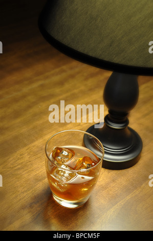 Bourbon sur les rochers sur table en bois éclairé par une lampe. Banque D'Images