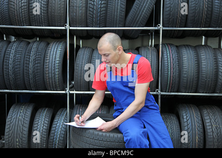 Un travailleur prend en inventaire un atelier de pneus et vérifie le stock. Banque D'Images