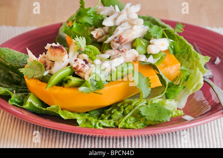 La papaye rempli de salade de crabe dormeur, pois sugar snap, et une garniture coriandre est servi sur un lit de laitue romaine. Banque D'Images