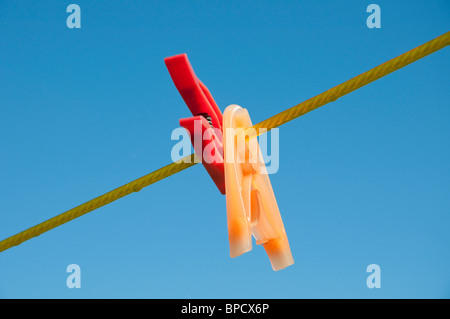 Le rouge et le jaune des pinces à linge sur une ligne, ciel bleu en arrière-plan Banque D'Images