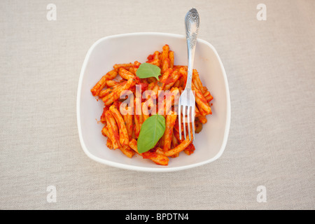 Pâtes Penne avec sauce marinara et feuille de basilic frais dans un bol blanc carré, fourchette sur le côté Banque D'Images