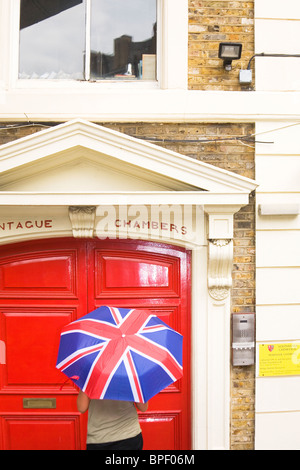 Femme frapper à une porte à Londres avec un Union Jack parapluie. Banque D'Images