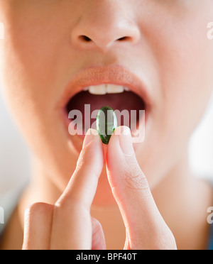 Mixed Race woman putting green capsule dans la bouche Banque D'Images