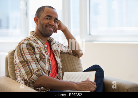 Mixed Race man sitting in armchair reading book Banque D'Images