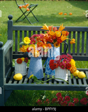 Still-Life de paille orange-fleurs et petits dahlias rouge dans les cruches en émail bleu sur banc de jardin en bois Banque D'Images
