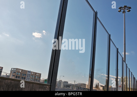 Cityscape déformée reflétée sur la surface tachée de la route de l'écran sonore. Banque D'Images