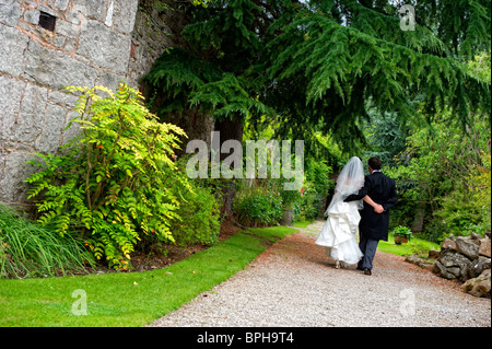 Mariée et le marié avec leurs bras autour de l'autre marche loin de la caméra le long d'un chemin de jardin Banque D'Images