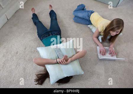 Hispanic teenager girl lying on floor avec oreiller et son ami à l'aide d'un ordinateur portable à côté d'elle Banque D'Images