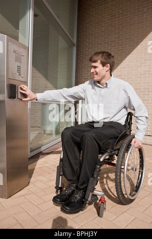 Businessman avec de la moelle épinière dans un fauteuil roulant en poussant un bouton pour ouvrir une porte Banque D'Images