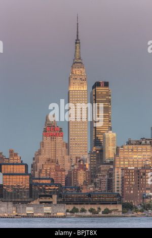 L'Empire State Building et Manhattan au crépuscule avec la lueur orange du ciel de l'ouest reflètent dans les fenêtres. Banque D'Images