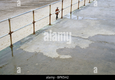 Promenade en béton avec de l'eau et la rouille des correctifs balustrades et figure ci-dessous la marche sur une large plage de sable vide Banque D'Images