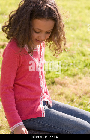 Petite fille assise sur l'herbe avec les cheveux bruns bouclés Banque D'Images