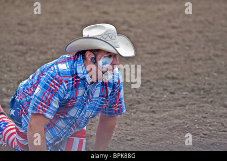 Ce rodeo cowboy est sur ses mains et les genoux dans la poussière. Il porte un chapeau de cowboy blanc et rouge, blanc et bleu 4e de juillet. Banque D'Images
