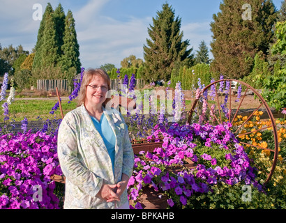 Smiling Caucasian cette femme d'âge moyen de l'équipement agricole rustique à l'arrière-plan de ce milieu rural, floral stock photo. Banque D'Images