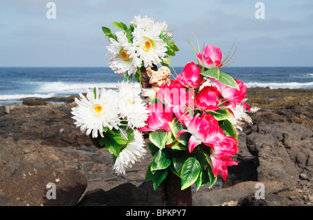 Ange et fleurs en plastique sur la croix de fer rouillée près de la mer Banque D'Images