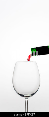 Vin rouge versé dans le verre contre fond blanc Banque D'Images