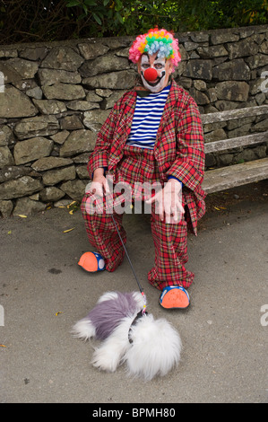 Clown assis sur un banc avec toy dog dans la rue au cours de l'époque Victorienne Llandrindod Wells Powys Pays de Galles UK Festival Banque D'Images