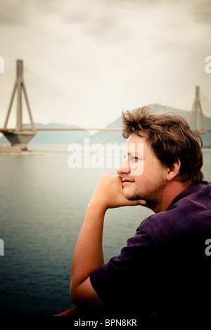 Jeune homme voyageant par bateau sur le golfe de Corinthe à admirer le pont de Rio, la Grèce. Banque D'Images