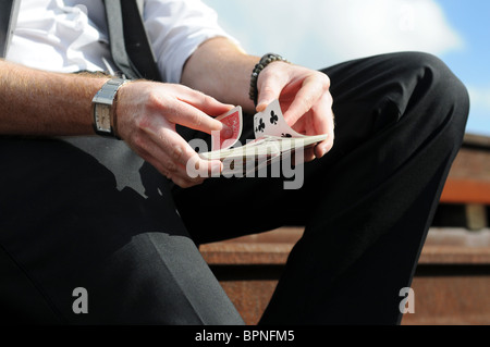 Les mains d'un jeune homme de race blanche magicien assis d'effectuer des tours de carte à l'extérieur Banque D'Images
