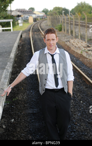 Jeune homme blanc magicien avec ginger hair posant dehors sur les voies de chemin de fer désaffectée Banque D'Images