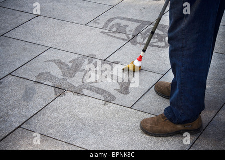 Un vieil homme chinois caractères brosses sur le plancher avec un gros pinceau. Banque D'Images