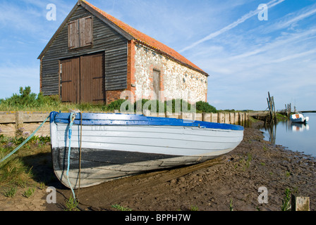 Planches en bois traditionnel bateau à rames à gauche sur des vasières à marée basse avec bâtiment de stockage avec en arrière-plan Banque D'Images