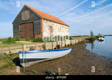 Planches en bois traditionnel bateau à rames à gauche sur des vasières à marée basse avec bâtiment de stockage avec en arrière-plan Banque D'Images