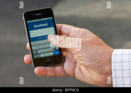 L'iPhone 4 dans la paume de la main d'un homme, montrant l'application Facebook login. Banque D'Images