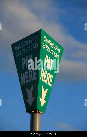 Poteau de signalisation dans un parking indiquant où payer et que des frais s'appliquent en tout temps. Banque D'Images