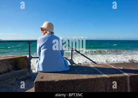 Femme âgée assise sur digue face à la mer Banque D'Images