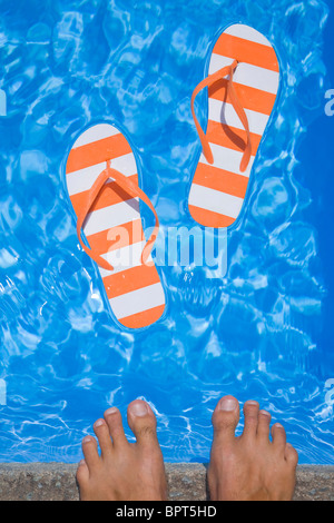 Jolie paire de tongs et de tongs stripey dans un bleu étincelant piscine avec les pieds d'un homme Banque D'Images