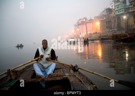 L'aviron de l'homme un petit bateau sur le Gange à Varanasi tôt le matin, de l'Uttar Pradesh, Inde. Banque D'Images