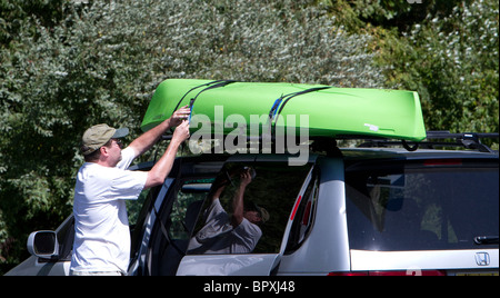 Un homme fixant son kayak sur le rack sur le dessus de son SUV wagon. Banque D'Images