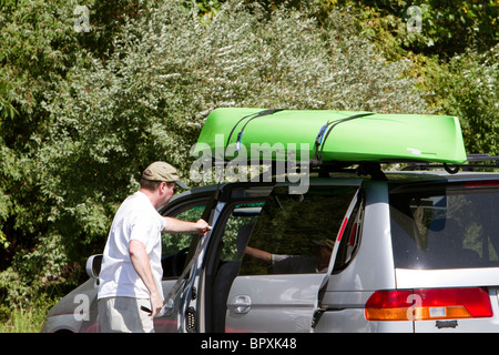 Un homme fixant son kayak sur le rack sur le dessus de son SUV wagon. Banque D'Images