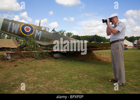 Un homme dans un bouchon blanc prend une photo à côté d'un avion Spitfire. Banque D'Images