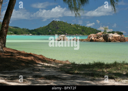 La baie de Anse Volbert à partir de l'ombre d'un arbre à travers la baie vers de lointaines maisons sur Praslin aux Seychelles Banque D'Images