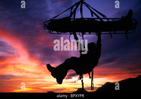 Recherche et sauvetage climber hanging from litière, sunset silhouette, Santa Barbara, CA Banque D'Images