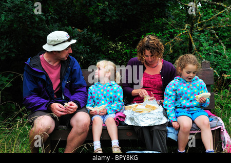 Famille assise sur un siège en bois avec de petits enfants en train de pique-nique, à Newtown, île de Wight, Angleterre Banque D'Images