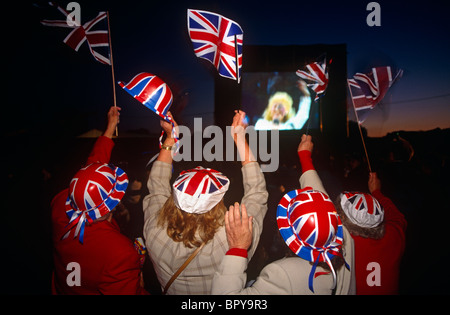 Quatre femmes sont vus de dos portant des chapeaux Union Jack et agitaient des drapeaux drapeau national de la Grande-Bretagne. Banque D'Images