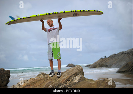 Un surfeur, Ben Howey, tenant un longboard de surf sur la plage de Fistral, Newquay, Royaume-Uni, la capitale du surf, à Cornwall Banque D'Images