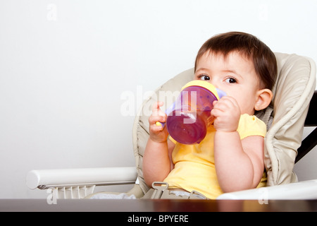 Mignon bébé enfant garçon fille sitting in chair de potable gobelet. Banque D'Images