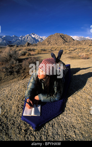 Une femme écrit dans son journal, tout en se trouvant sur son couchage tôt le matin tout en camping dans le désert. Banque D'Images