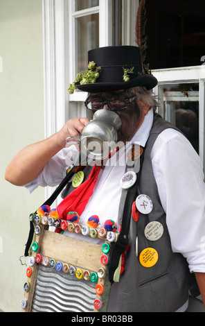 Un danseur de Morris à la caméra au visage noirci avec bénéficie d'une pinte de bière d'un tankard au festival hop Faversham Banque D'Images