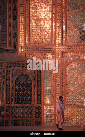 Un homme marche sous un mur de mosaïque tuile rougeoyante, à la Mosquée Bleue complexe, Mazar-i Sharif Banque D'Images