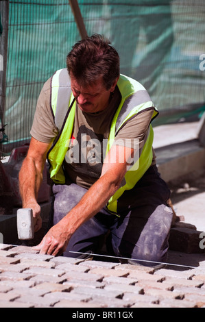 L'homme au travail pose de nouvelles boutures de cobblestone paving scheme, Hereford, Royaume-Uni. Construction Worker building trottoir avec blocs de pierre Banque D'Images