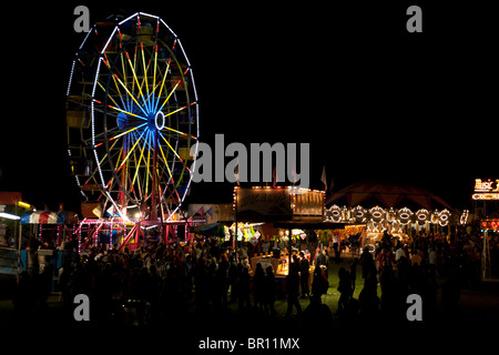Soirée à la foire. À propos d'un moulin Fairgoers carnaval voyager après la tombée de la nuit le jour de la fête du Canada. Une grande roue est bien éclairée Banque D'Images