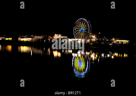 Carnaval de nuit de réflexion. À propos d'un moulin Fairgoers carnaval voyageant sur la fête du Canada. Une grande roue se reflète Banque D'Images