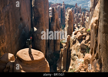Un homme debout sur le socle rocheux à la recherche à afficher dans le bas du canyon rock formations, Arches National Park, Moab, Utah. Banque D'Images